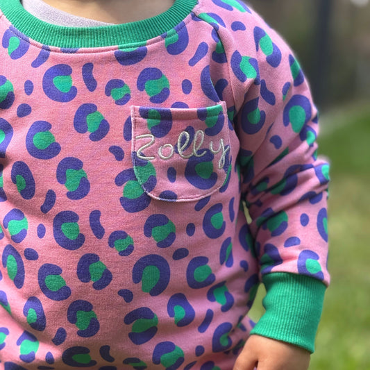Kids' pink leopard print sweatshirt with green accents and 'Zolly' embroidered pocket detail.