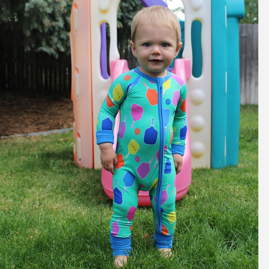 Toddler wearing a colorful green one-piece romper with playful bottle print, ideal for playtime.