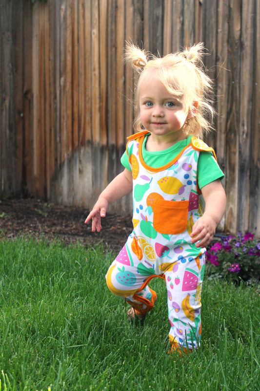 Colorful children's romper with fruit prints, green sleeves, orange pocket, and comfy fit for playing outdoors.