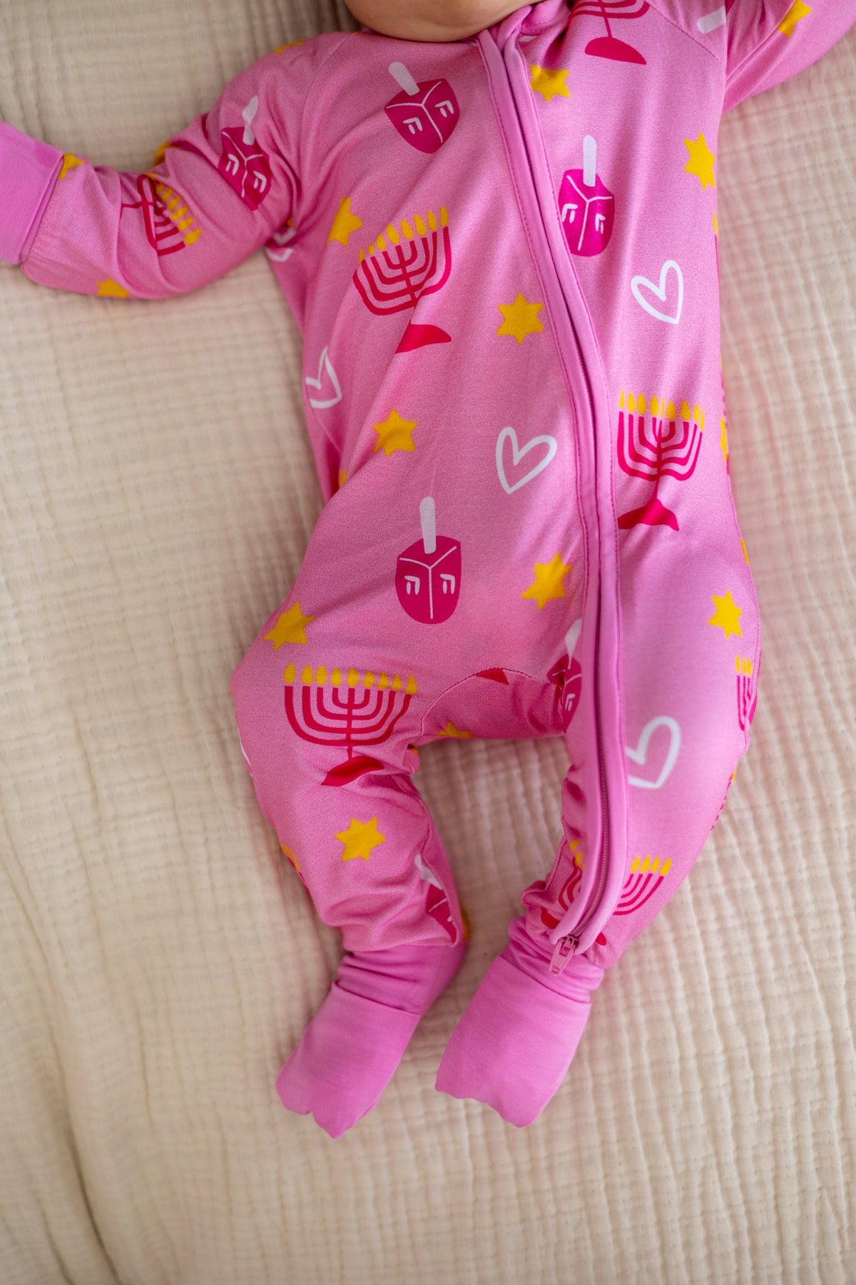 Cute pink baby onesie with menorah and dreidel print, soft material, ideal for celebrations and cozy wear.