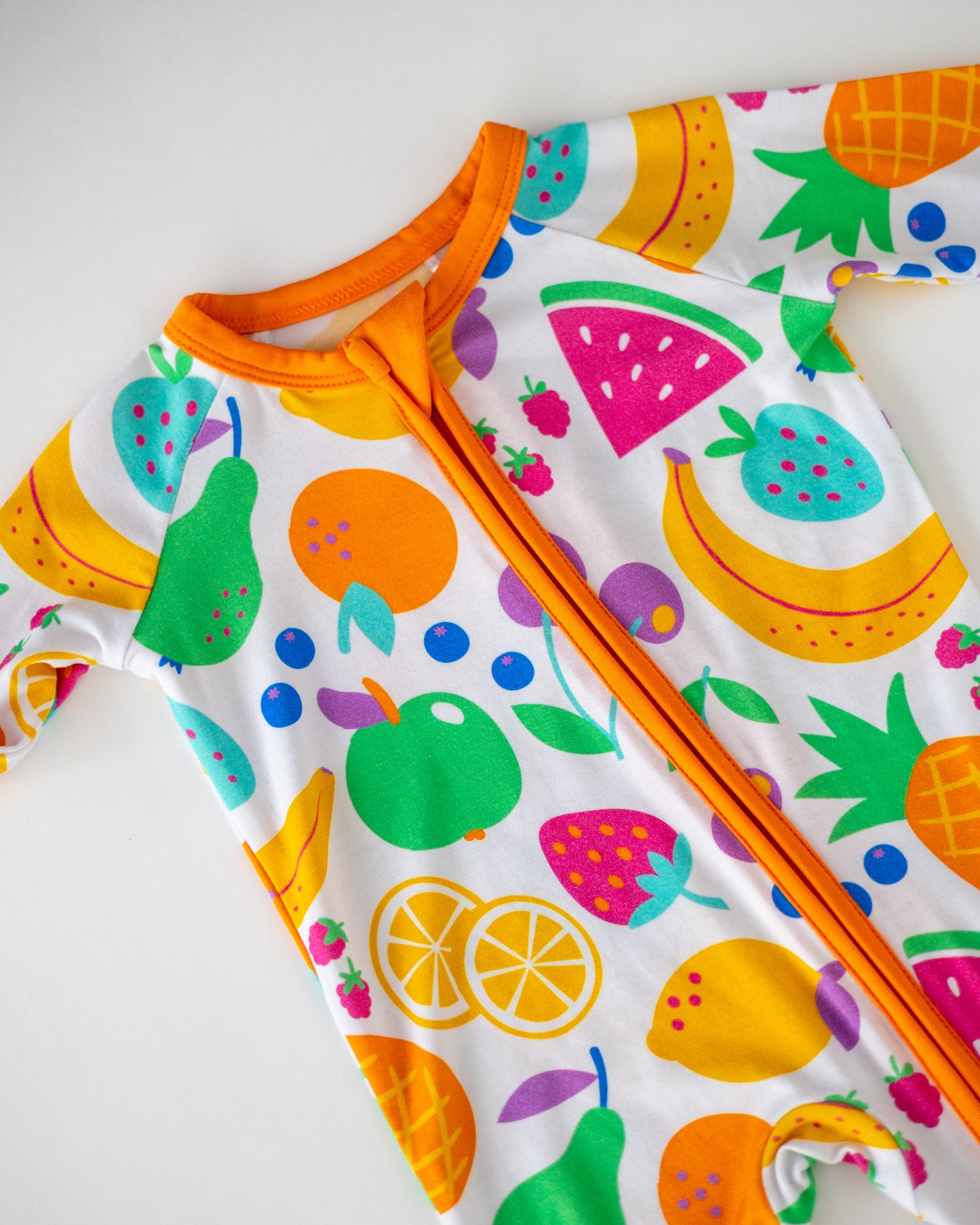 Colorful fruit-patterned baby onesie with orange trim, made from soft, breathable cotton.