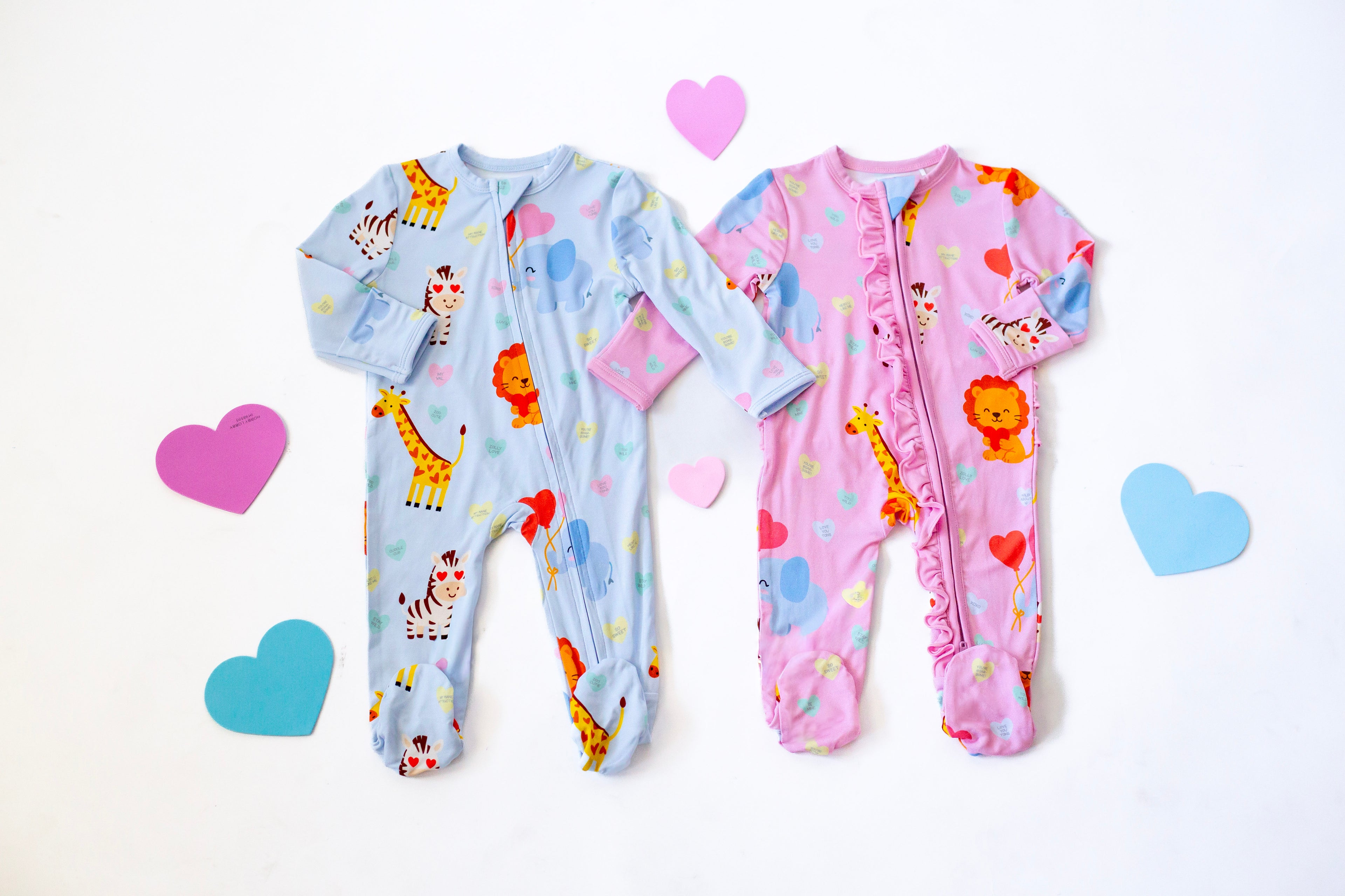 Two baby onesies, one blue with animal prints and one pink with heart patterns, on a white background.