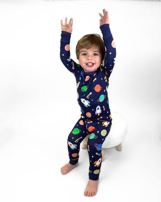 Navy blue kids' pajamas with colorful space theme, featuring rockets and planets, made of soft breathable material.