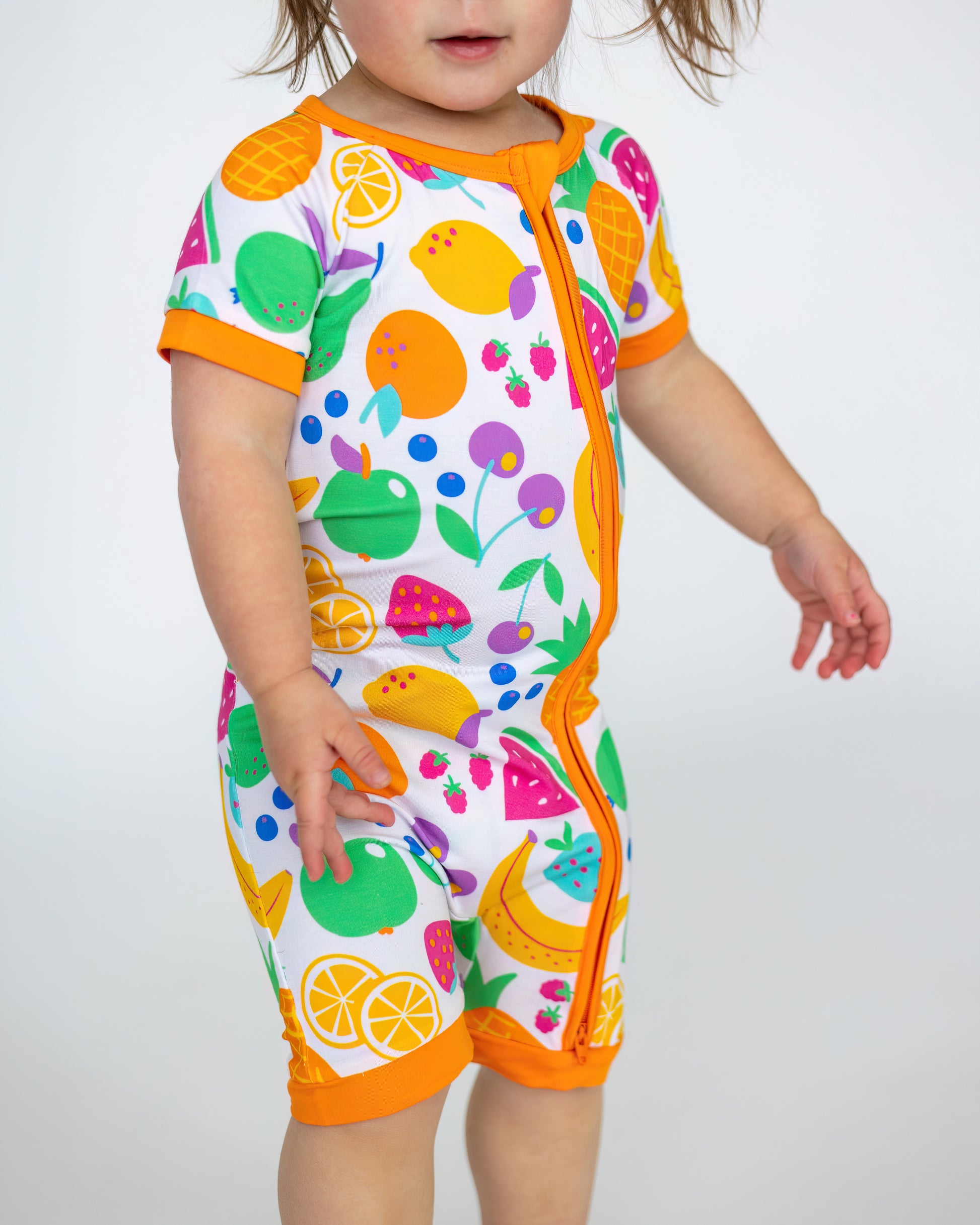 Colorful toddler onesie featuring fruit patterns, short sleeves, and orange accents, made from soft fabric.