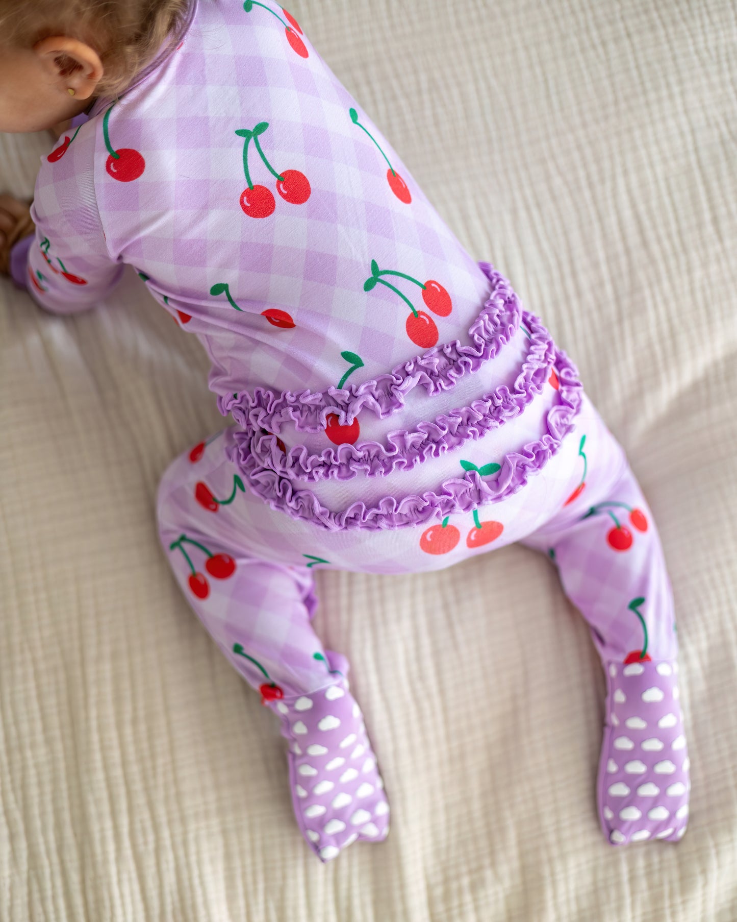 Cute toddler pajamas in light purple with cherry print, featuring ruffled back and footed design.