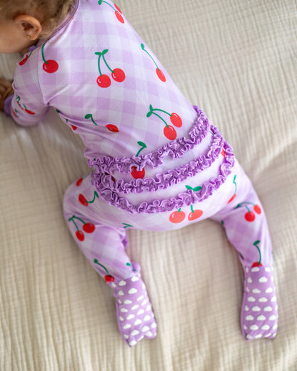 Cute toddler pajamas in light purple with cherry print, featuring ruffled back and footed design.