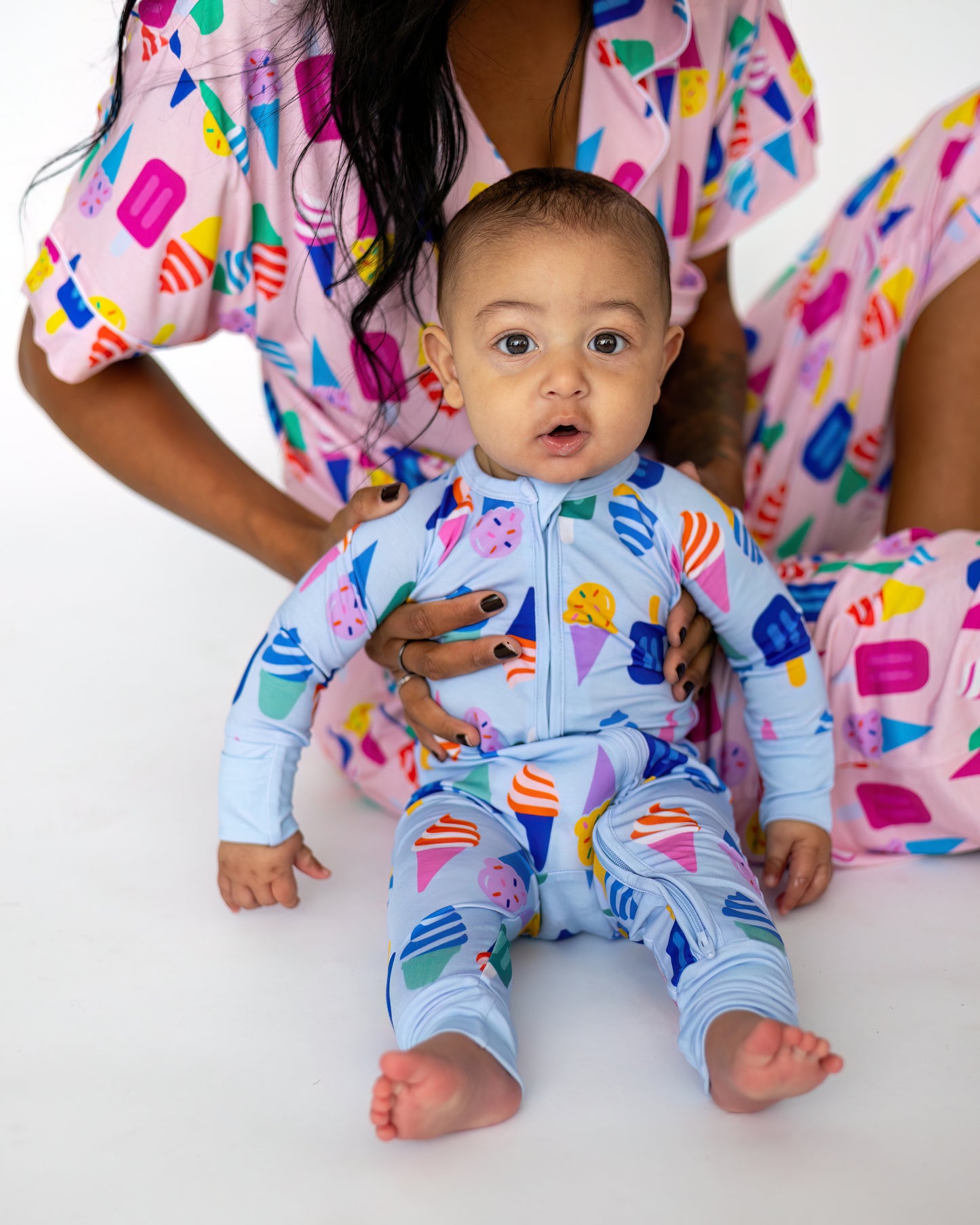Baby in light blue ice cream patterned onesie, sitting with parent in matching colorful loungewear.