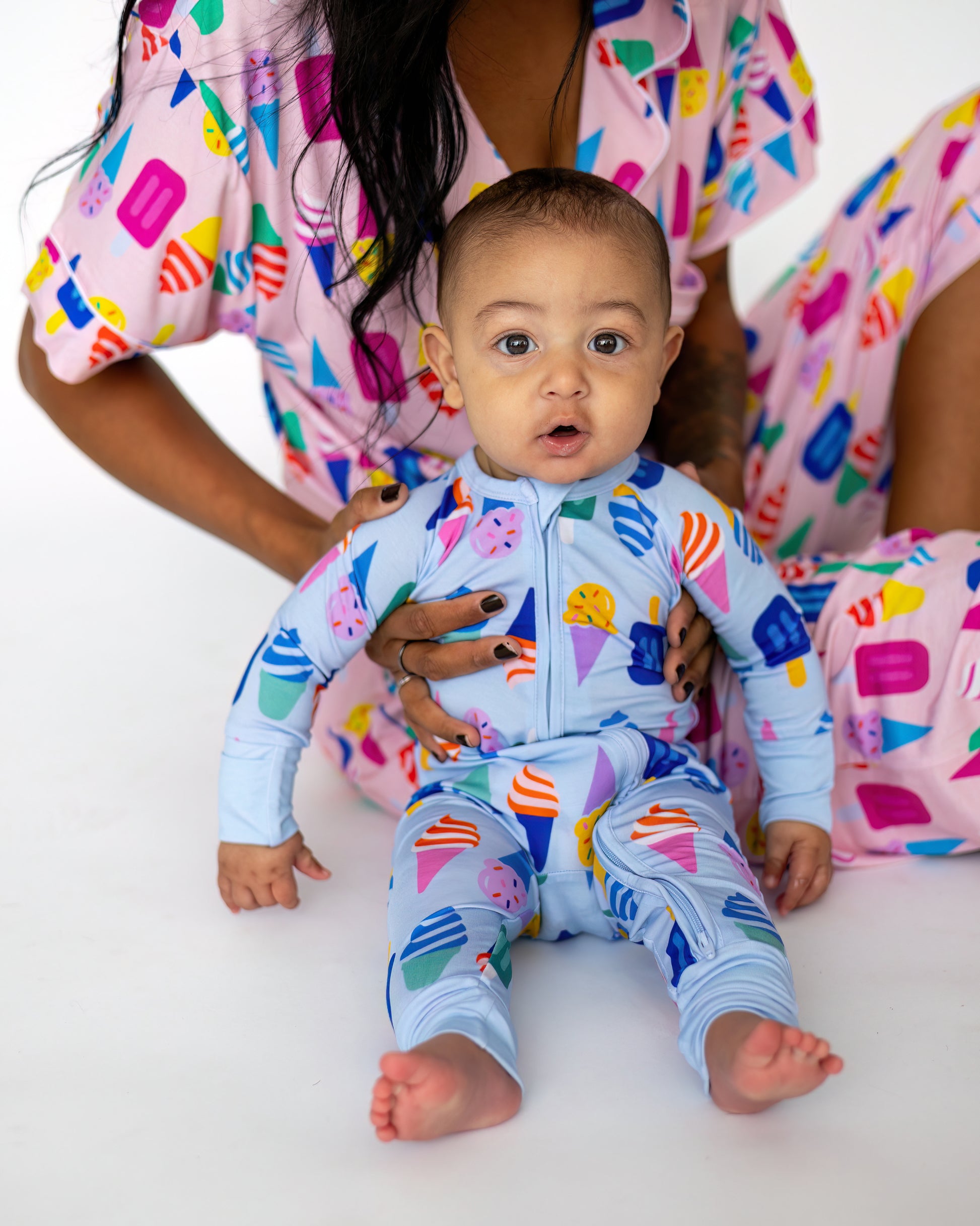 Baby in light blue ice cream patterned onesie, sitting with parent in matching colorful loungewear.