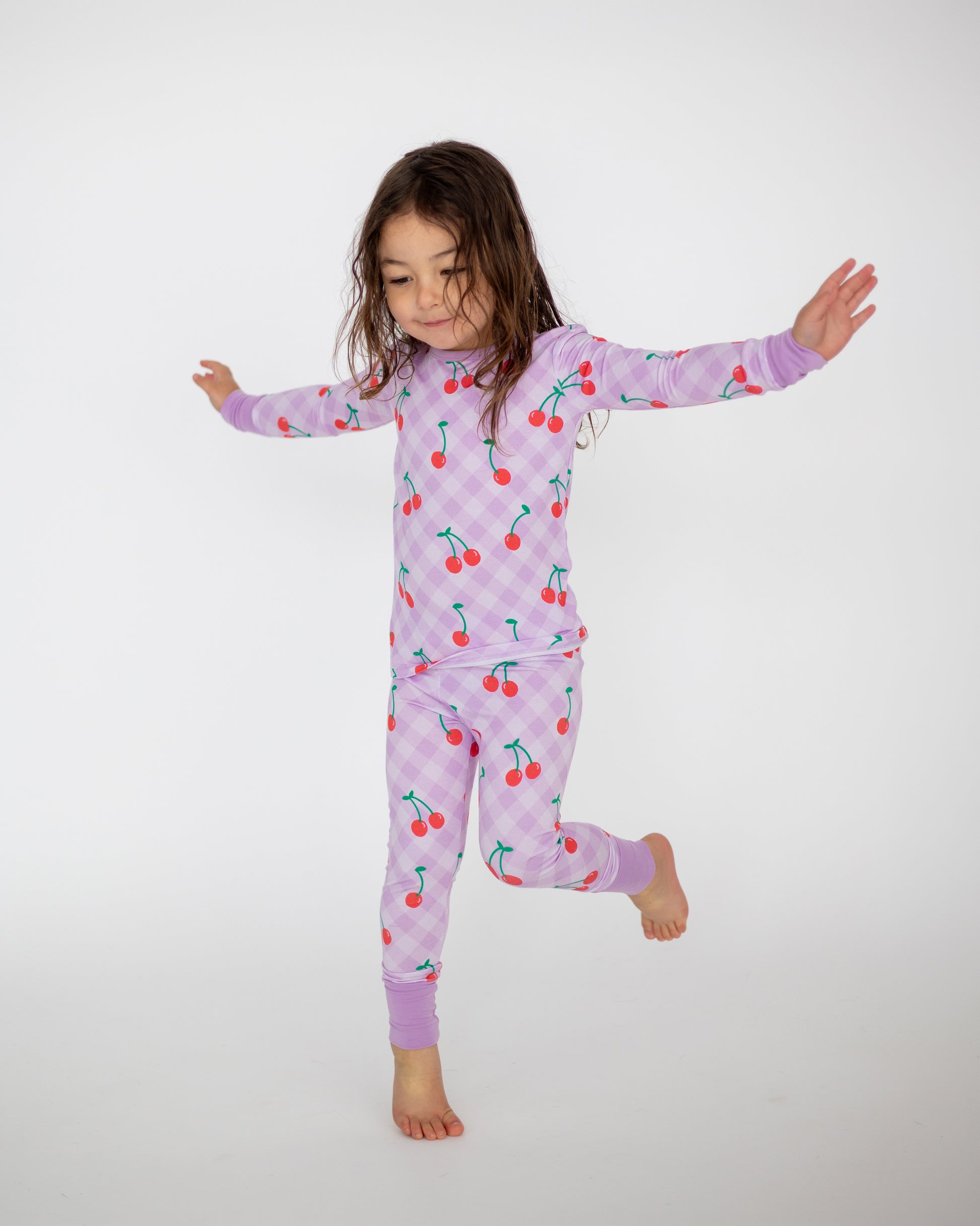 Girl in cherry print purple pajamas made from soft, breathable cotton, perfect for cozy nights.