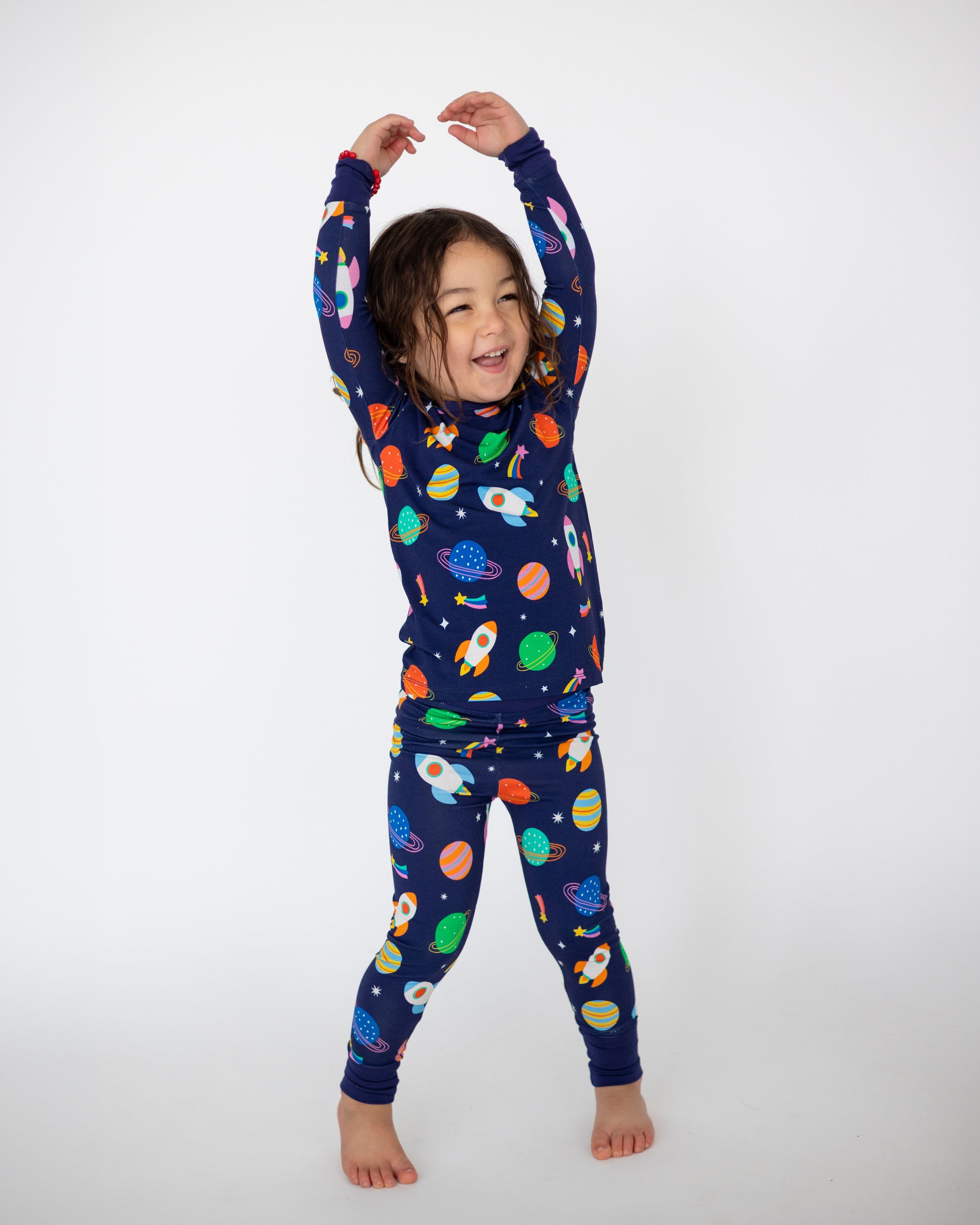 Kids' navy blue space-themed pajamas featuring rockets and planets, made from soft, stretchy fabric.