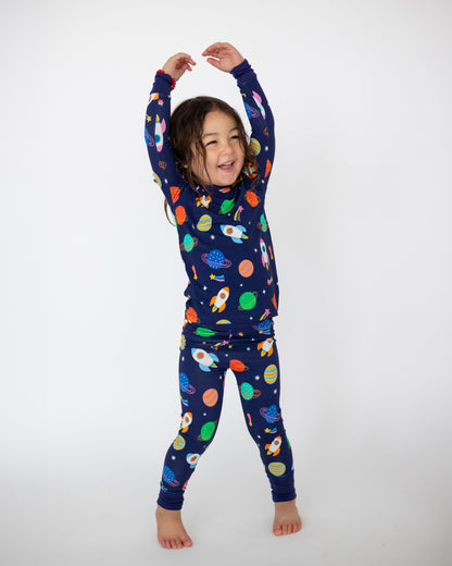Kids' navy blue space-themed pajamas featuring rockets and planets, made from soft, stretchy fabric.