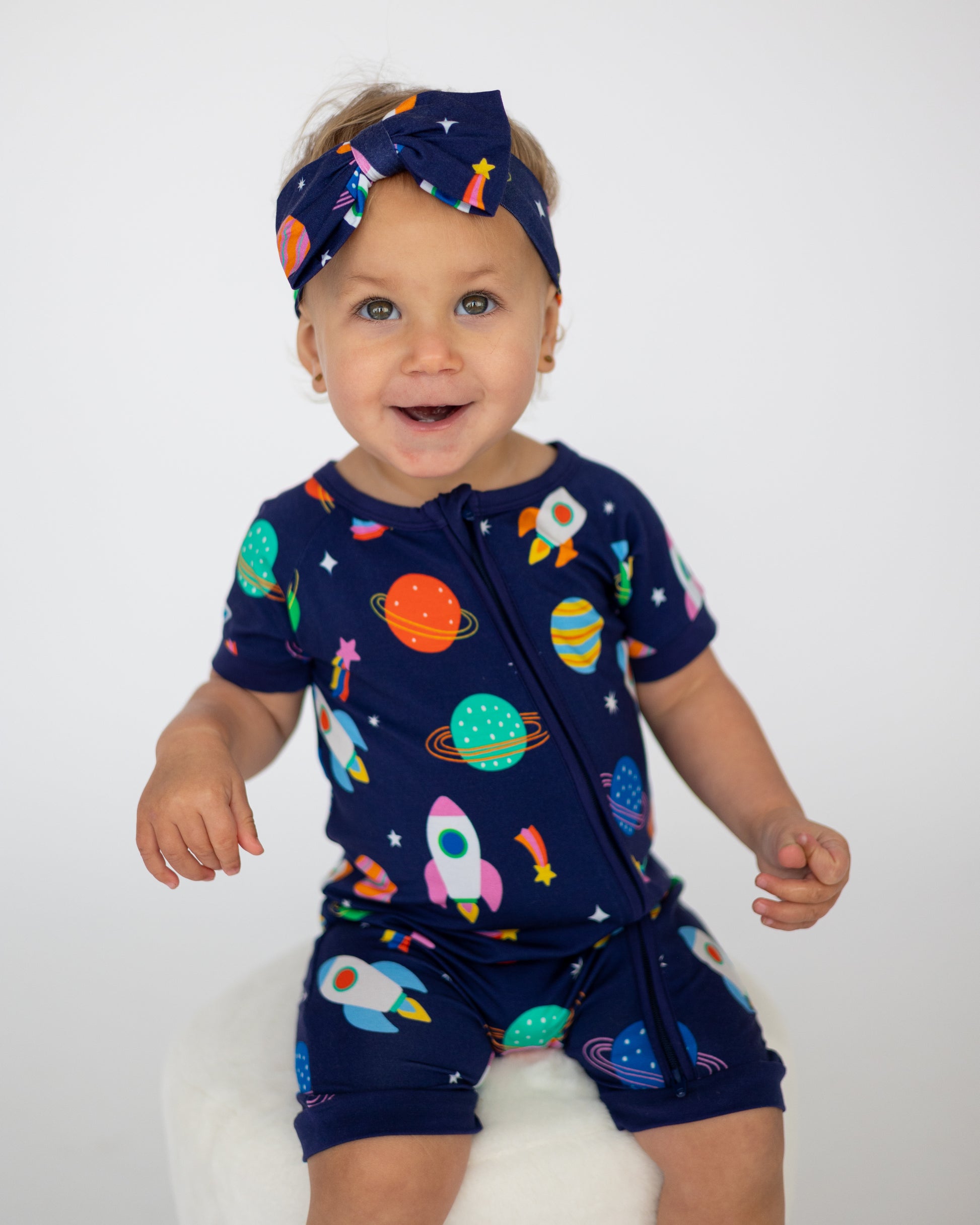 Baby romper set in navy blue with colorful space-themed prints and matching headband, perfect for play.