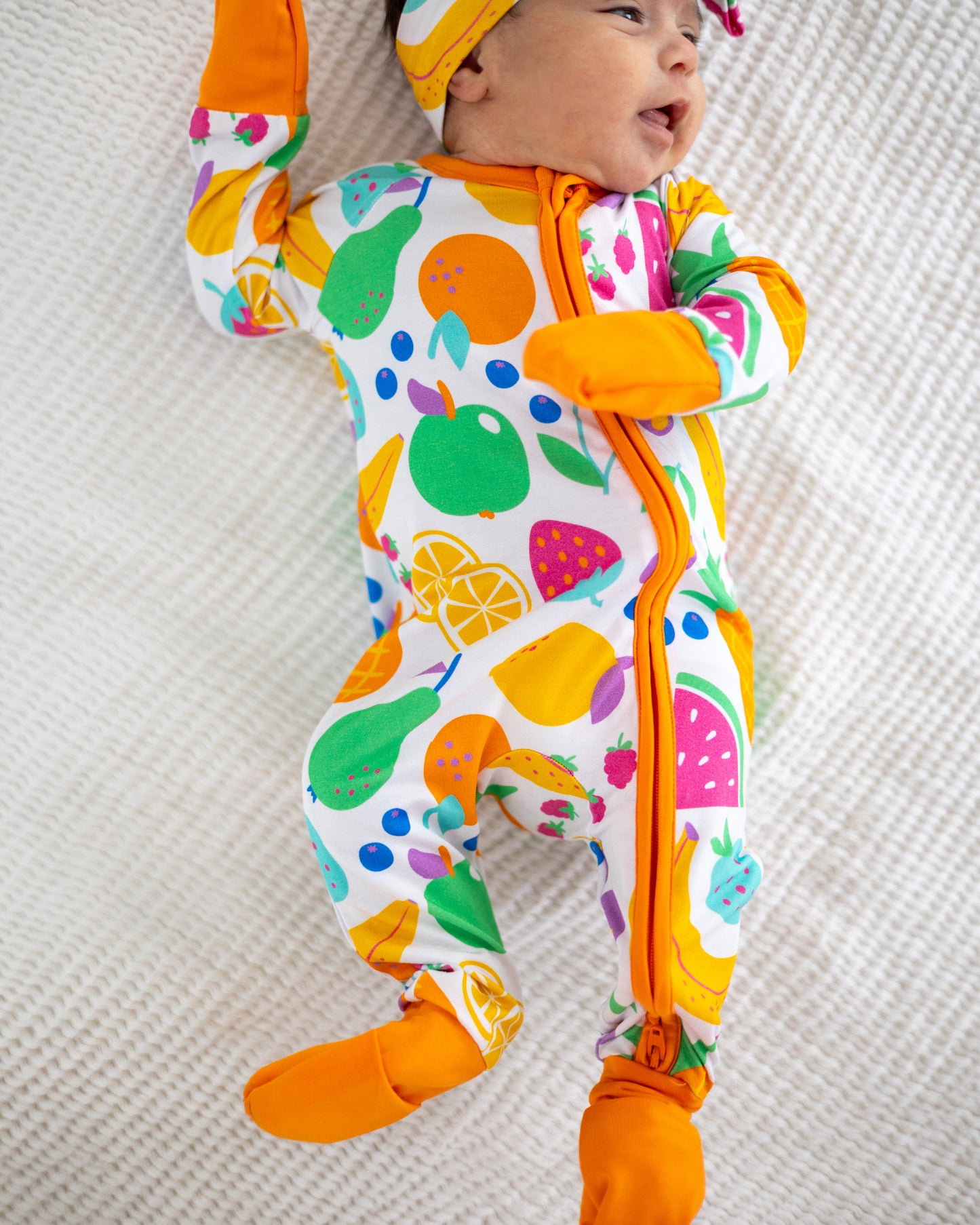 Colorful fruit-patterned baby onesie with orange trim and zipper for easy dressing.