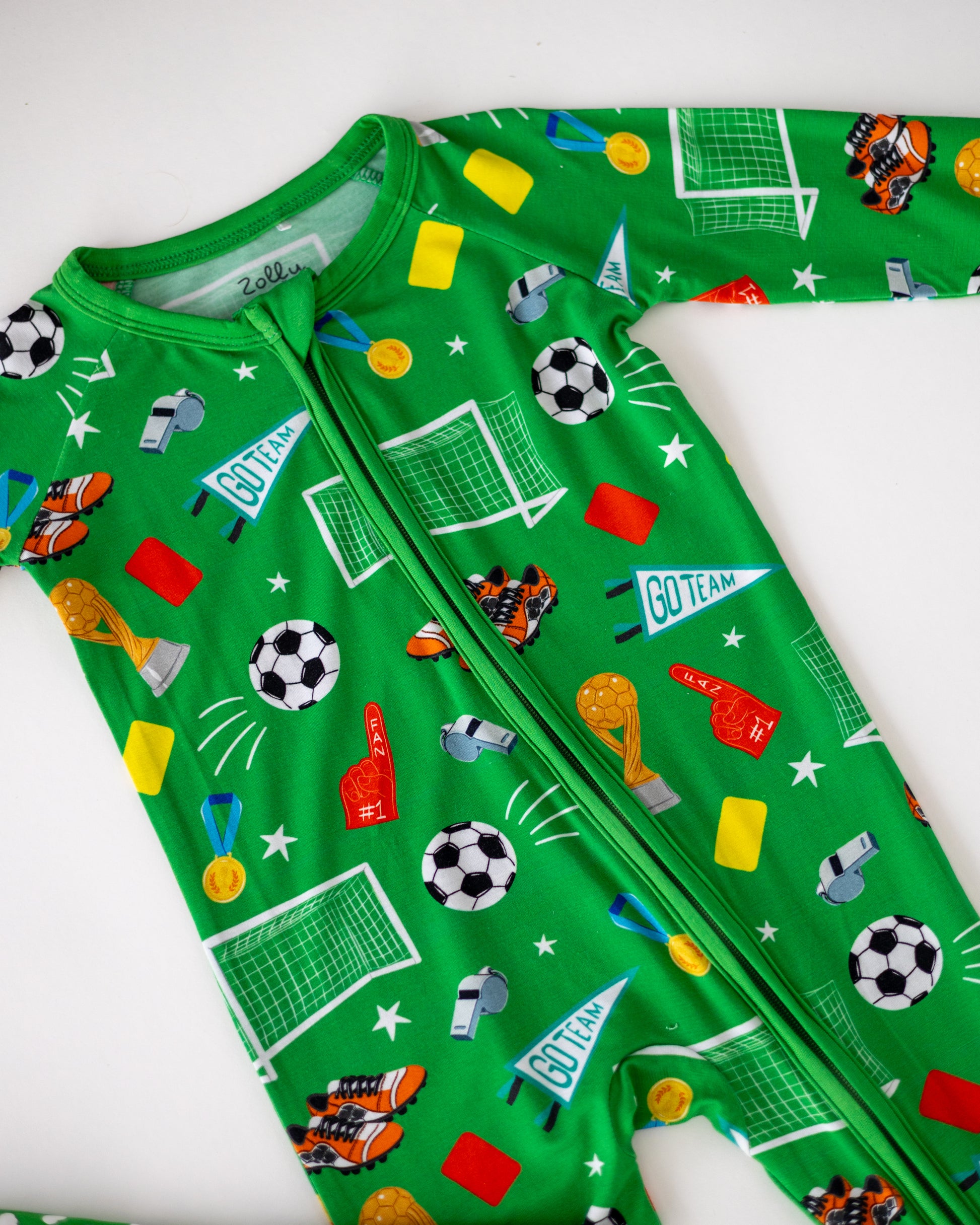 Green soccer-themed onesie with fun prints of balls, trophies, and sports gear for kids.