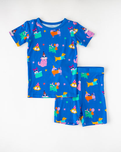 Colorful kids' short pajamas set, featuring playful dog and cat designs on blue fabric.