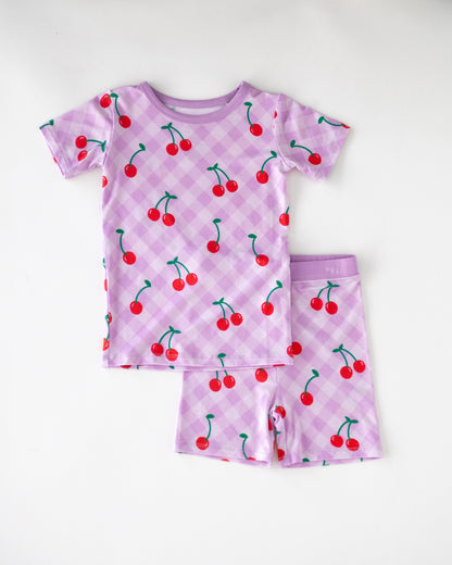 Children's purple cherry print pajamas set, short sleeve top and shorts, made from soft breathable fabric.