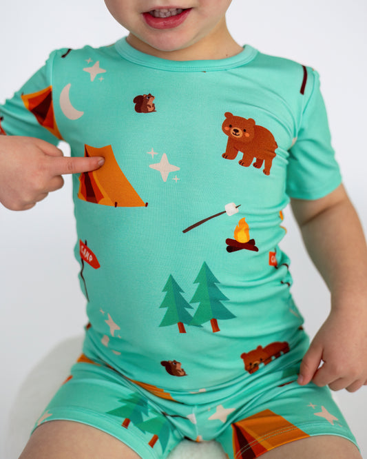 Kids' turquoise camping-themed pajamas with bear and tent prints, made from soft, breathable material.