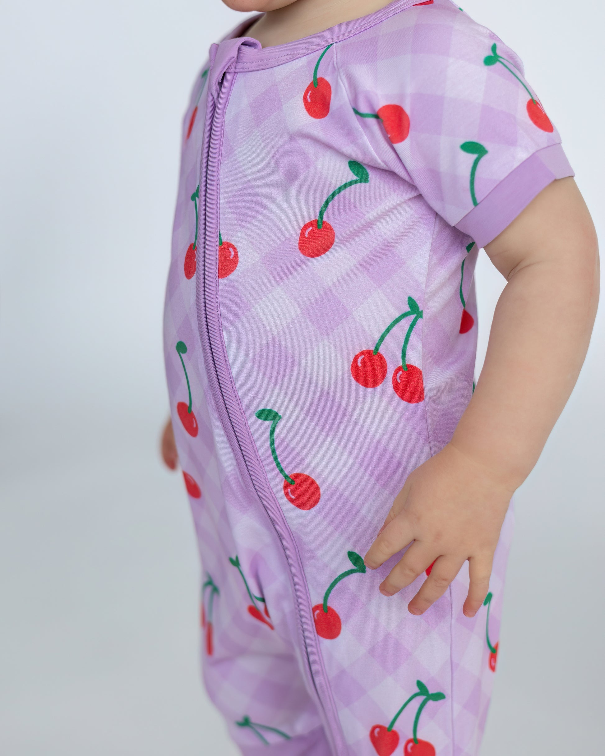 Purple gingham baby romper with cherry print, short sleeves, and front zipper for easy dressing.
