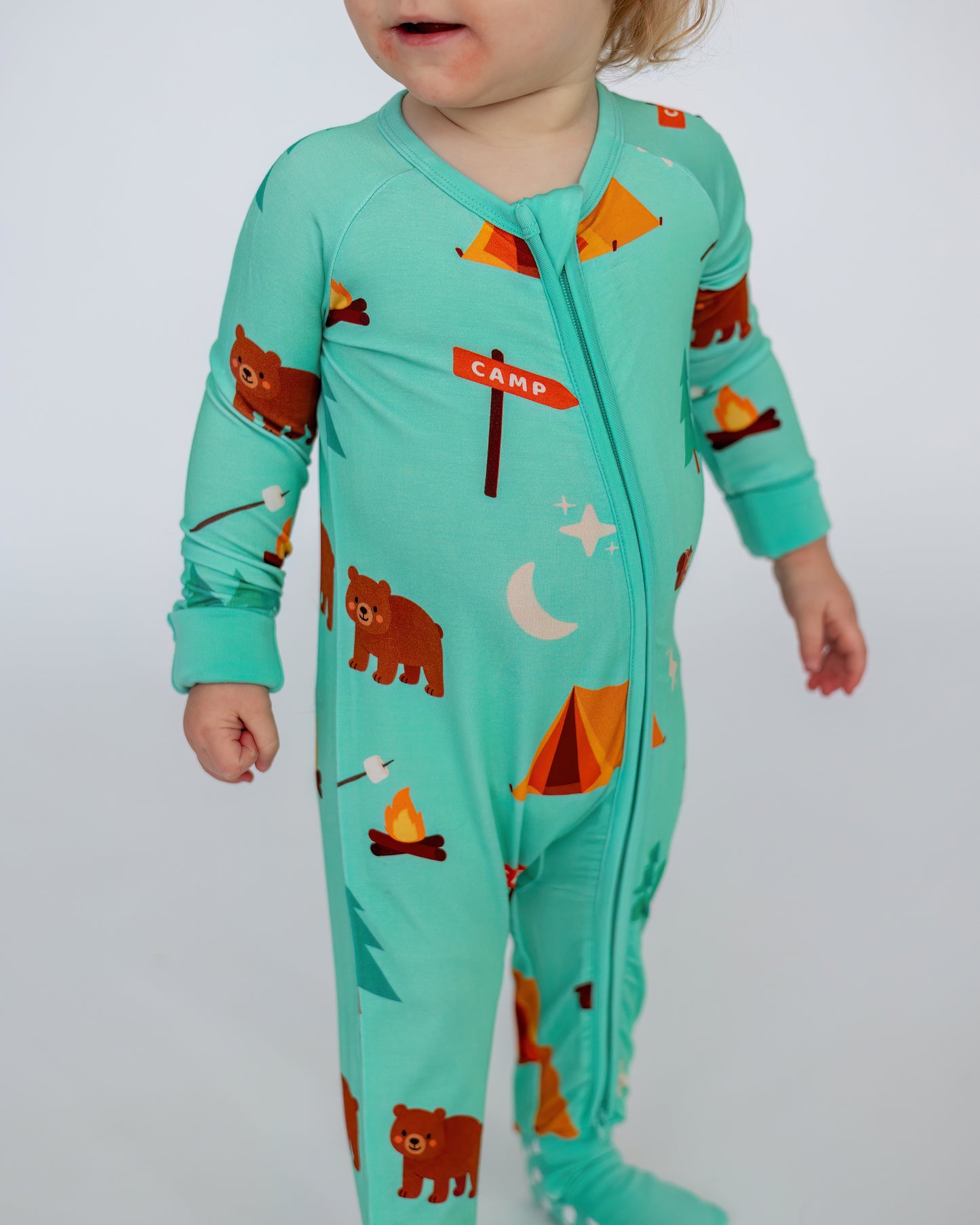 Kids' teal camp-themed onesie with bear, tent, and campfire prints, made from soft, breathable fabric.