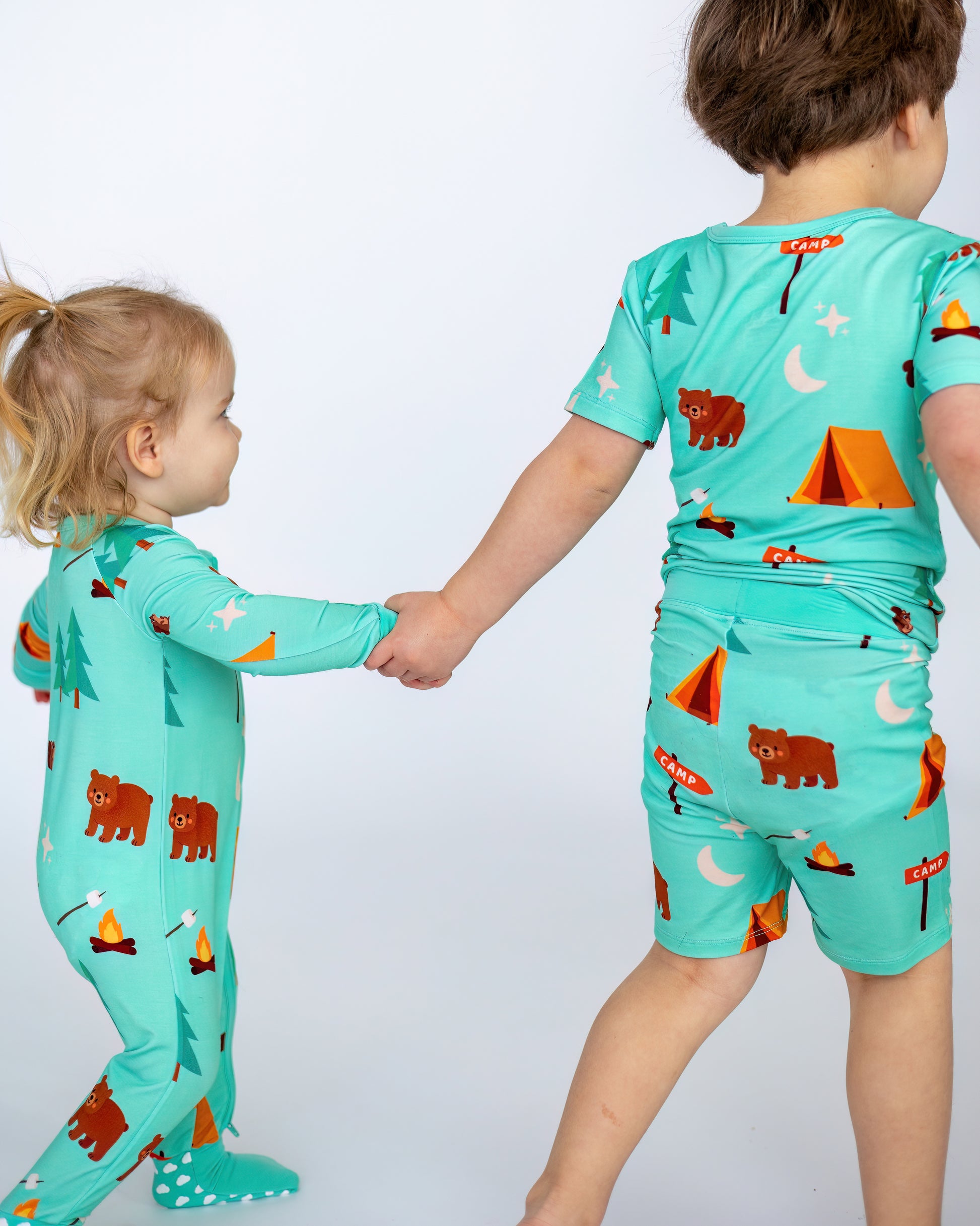 Matching kids' camp-themed pajamas, turquoise with bears and tents, perfect for fun sleepovers.