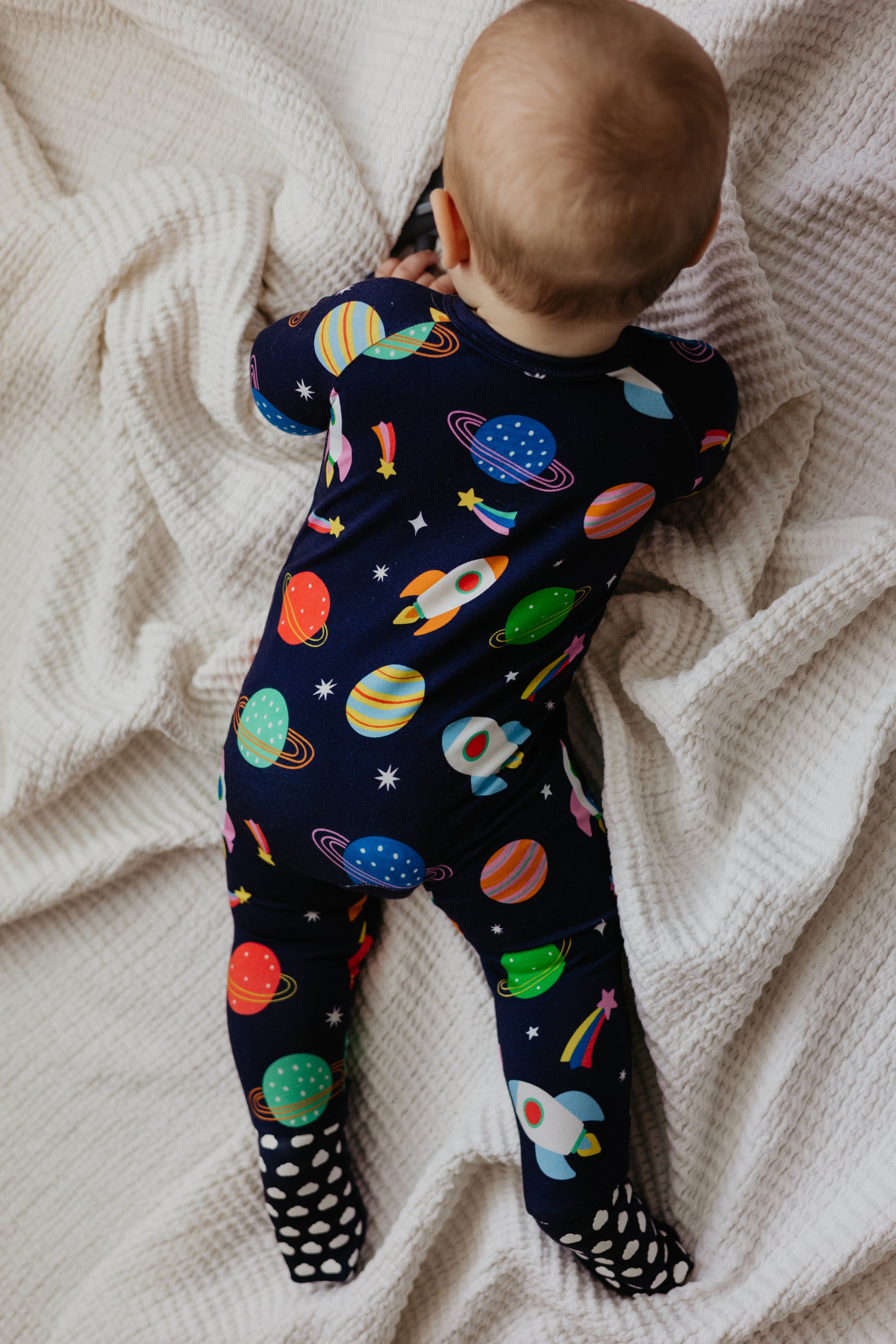 Baby's navy space-themed romper with colorful planets and rockets, featuring soft fabric and polka dot feet.